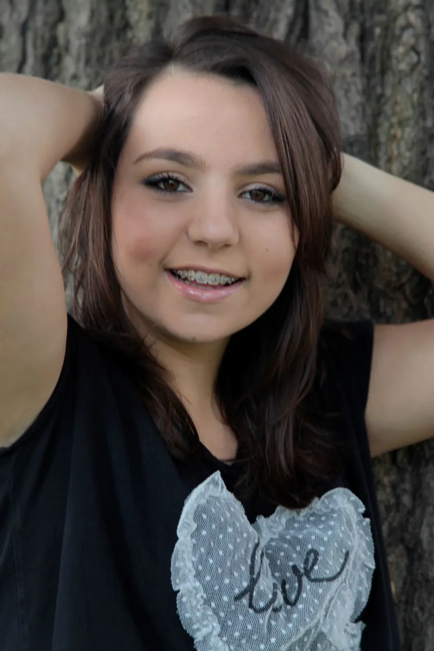 Senior portrait of a young woman leaning against a tree in soft daylight
